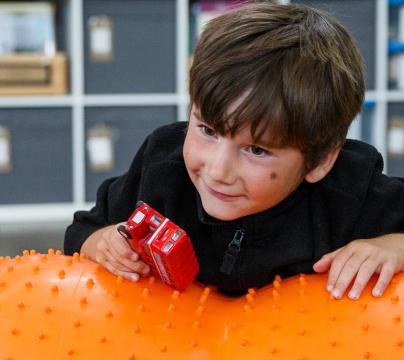 Boy on orange inflatable toy holding a toy bus
