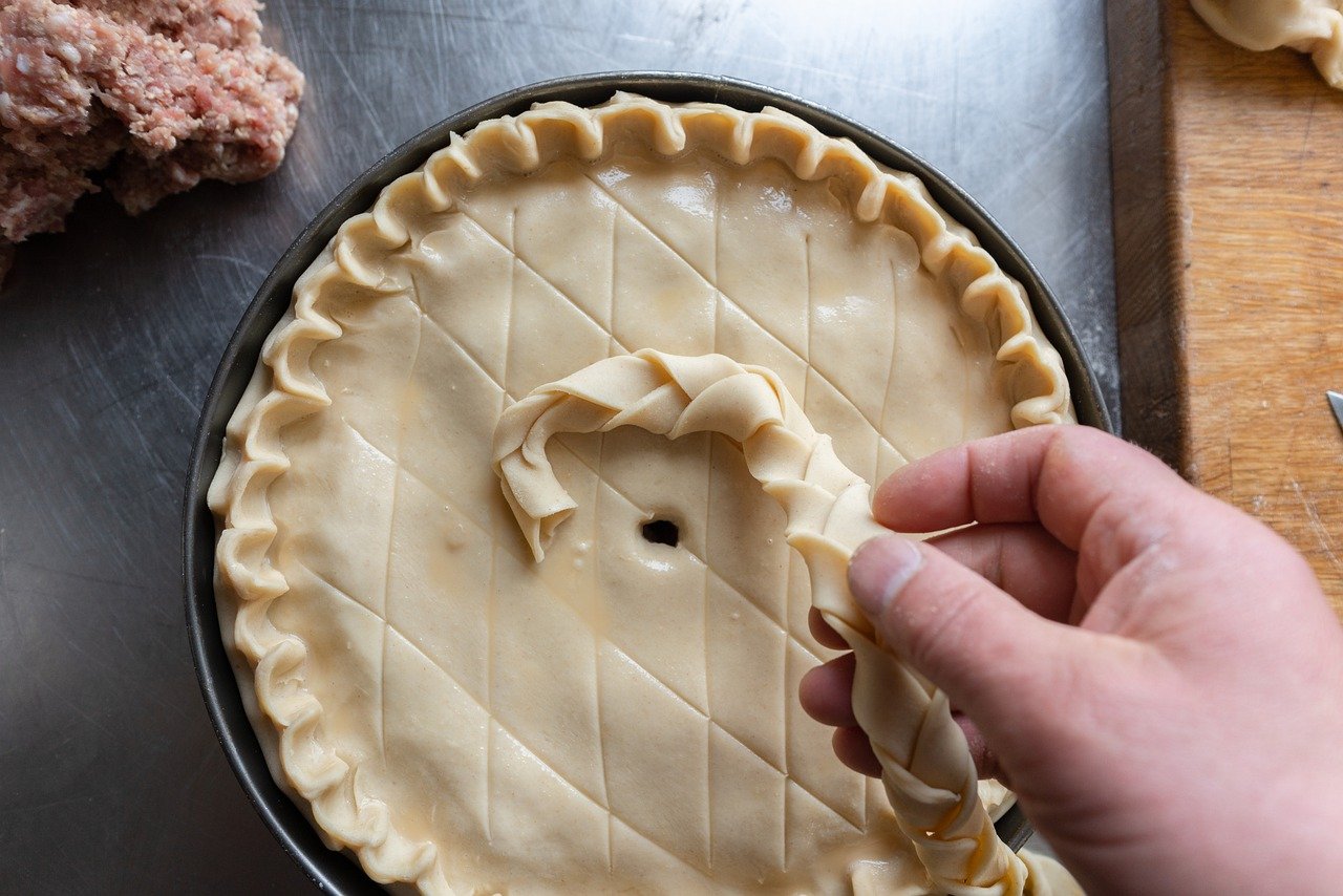 Finishing decorating Traditional Pork Pie on metal table