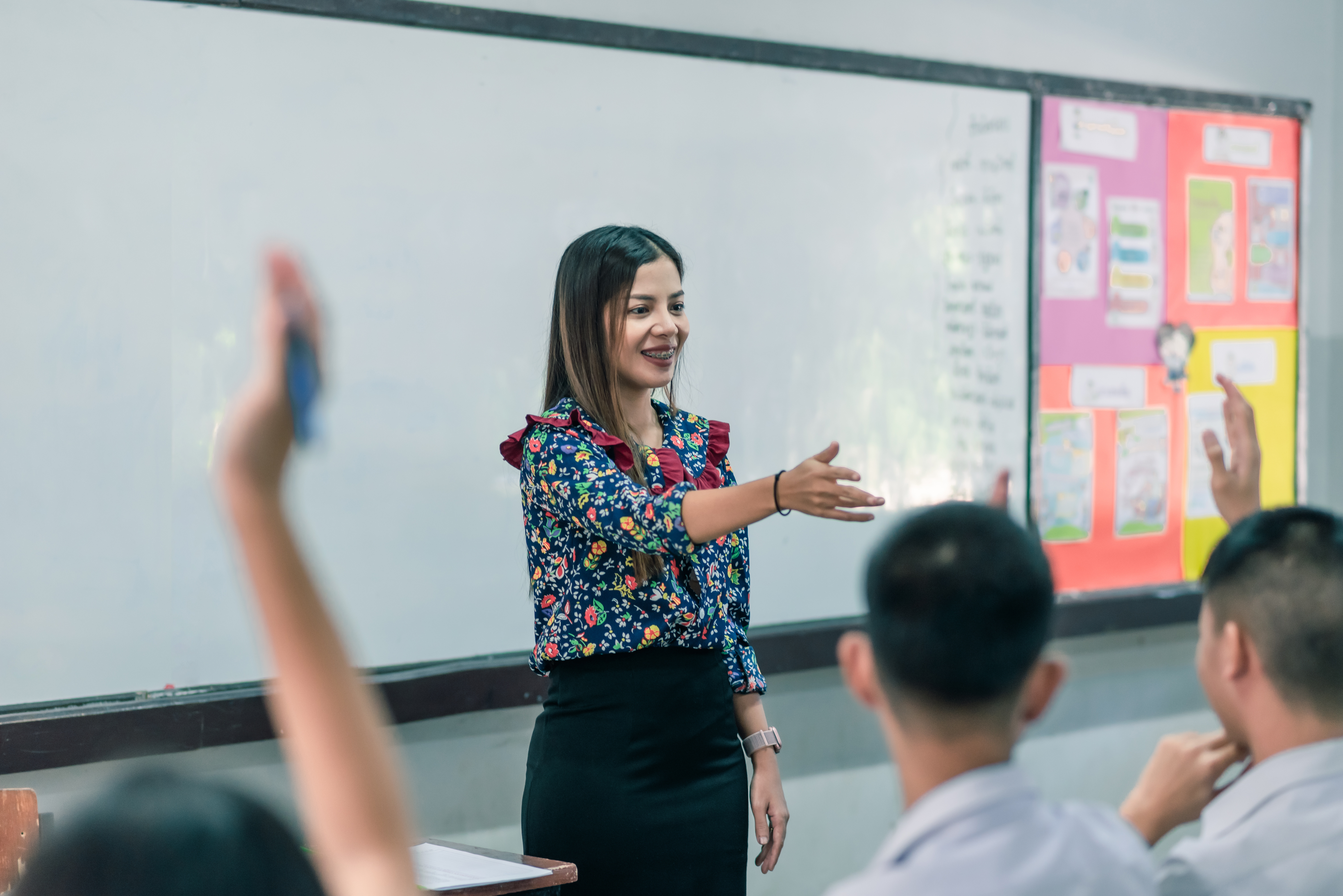 Woman holding out her hand in front of classroom and whiteboard