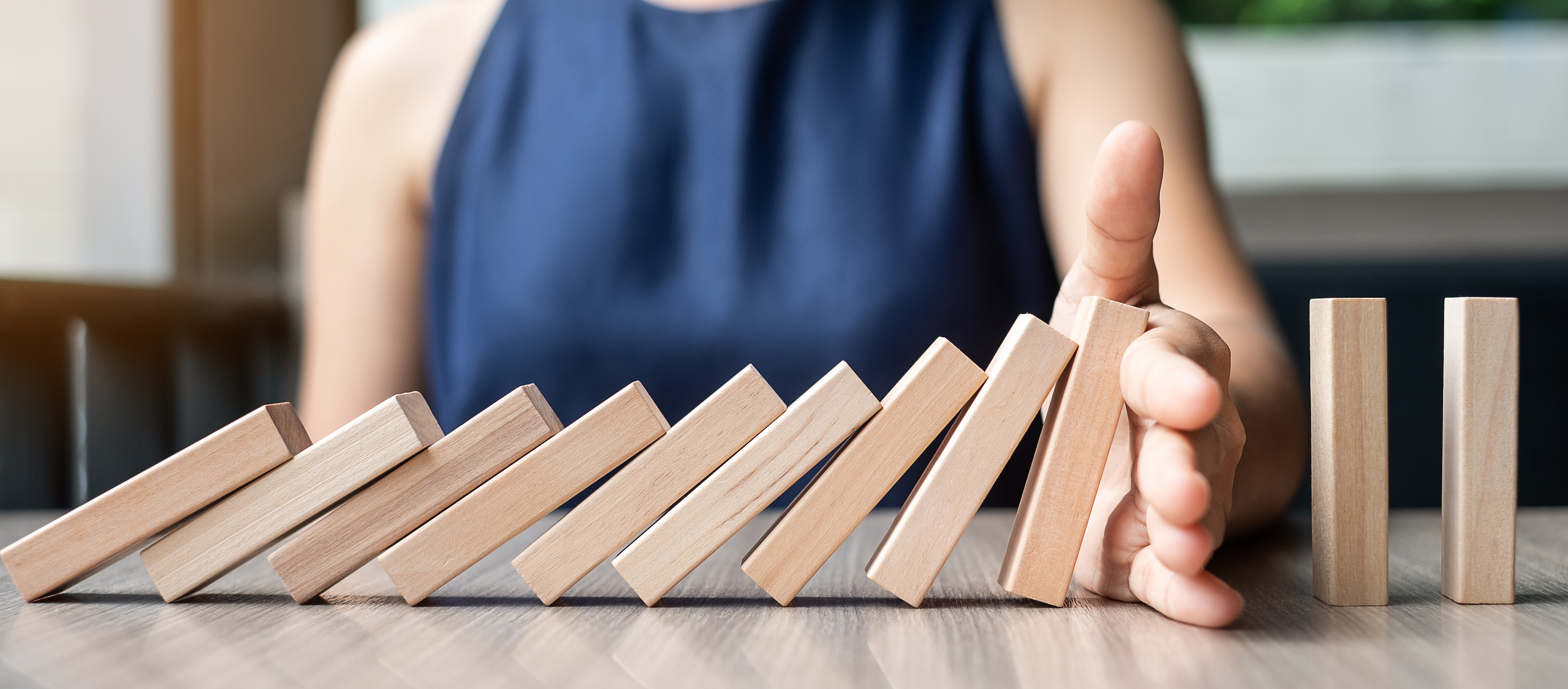 Hand being used to stop dominoes from falling