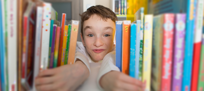 Child peeking through books on a shelf