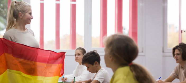 Adult holding a rainbow flag at the head of a classroom
