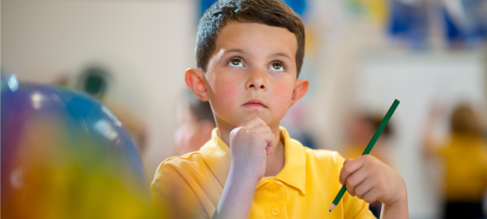Thoughtful looking child in yellow shirt, holding pencil 