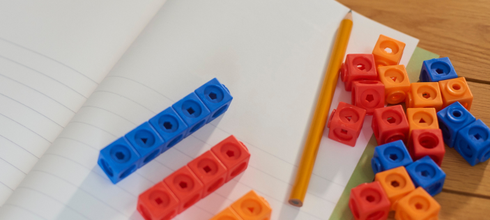 Orange and blue counting blocks with yellow pencil and white lined paper on a wooden desk