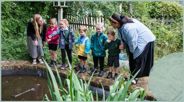 children and teachers round a pond